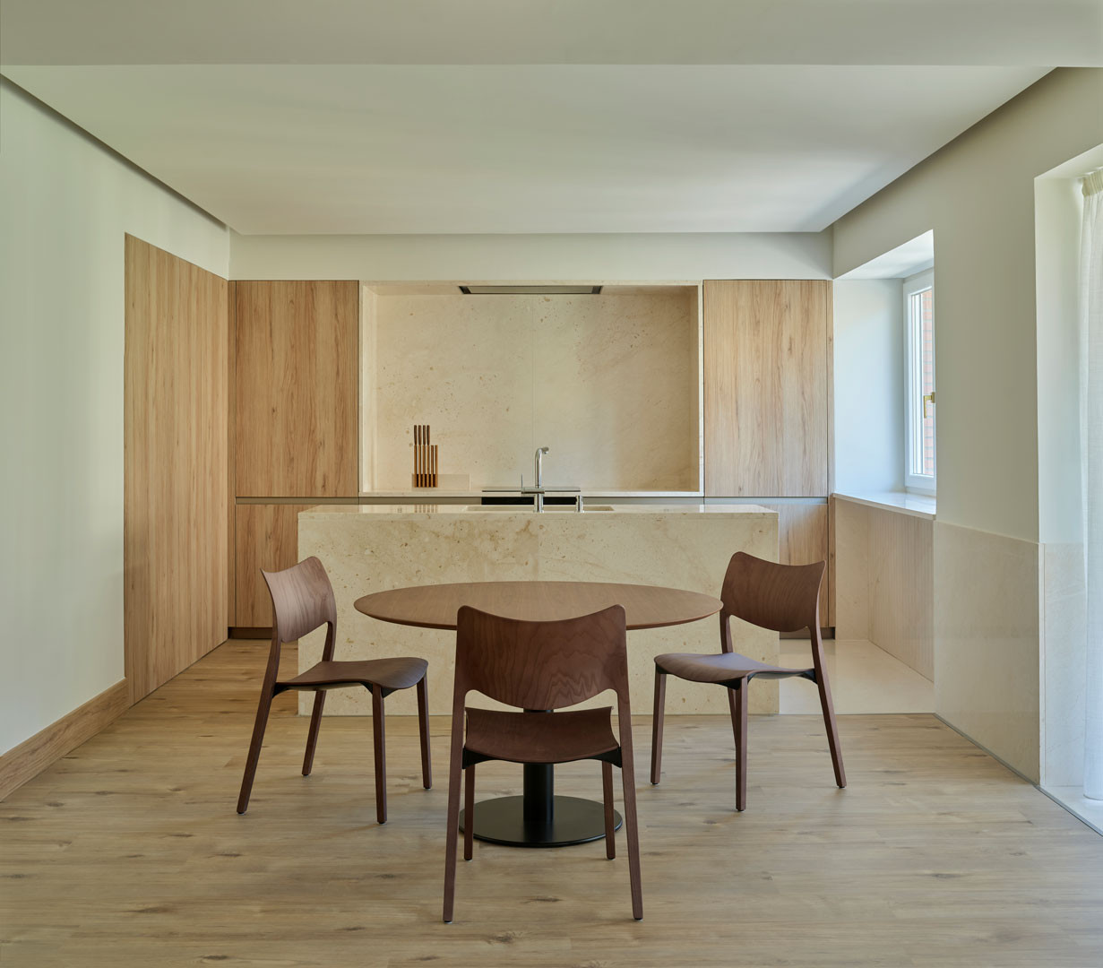 Comedor con mesa y sillas ante la cocina de madera del apartamento Calasanz