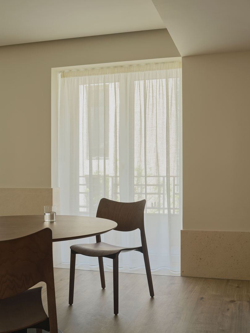 Mesa y silla de madera junto a una ventana con cortinas en el apartamento Calasanz
