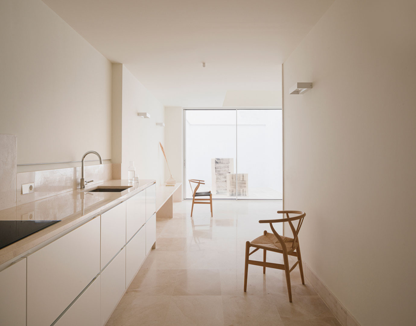 Cocina y estancia continua de planta baja de Casa Mirasol, con encimera de piedra y silla de madera